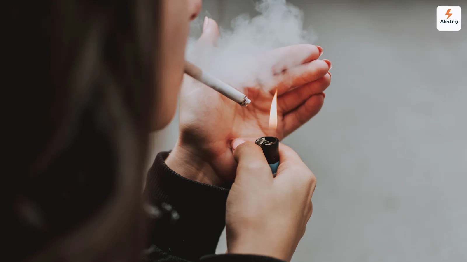 Άτομο ανάβει τσιγάρο σε εσωτερικό χώρο με τον καπνό να τυλίγεται γύρω από τα χέρια του