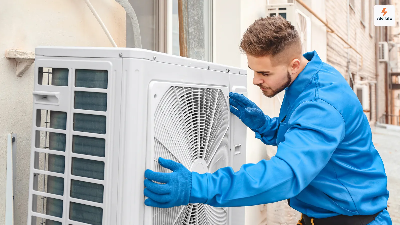Τεχνικός HVAC με μπλε φόρμα και γάντια κάνει συντήρηση σε εξωτερική μονάδα κλιματισμού
